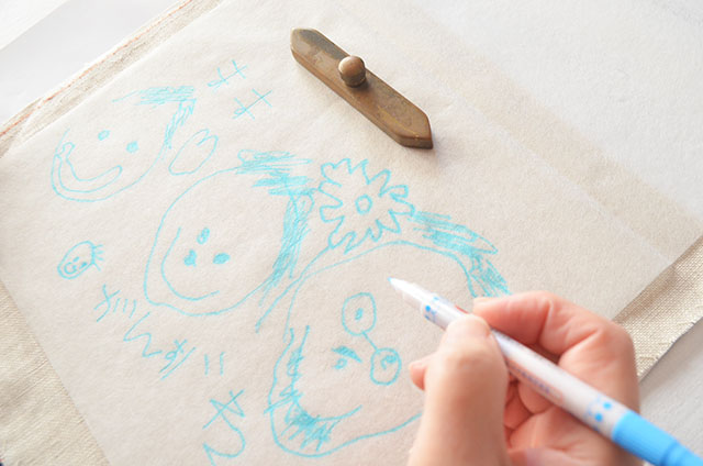 作業工程：写真からトレースしたアートラインを刺繍布（麻布）へ写す。子供の描いた絵を忠実に再現するために重要な工程。